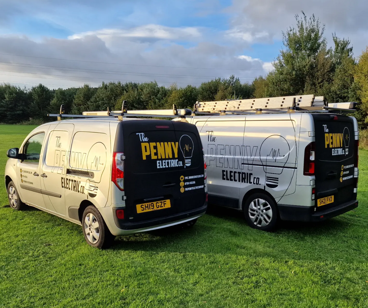 Two branded Penny Electric vans parked on grass